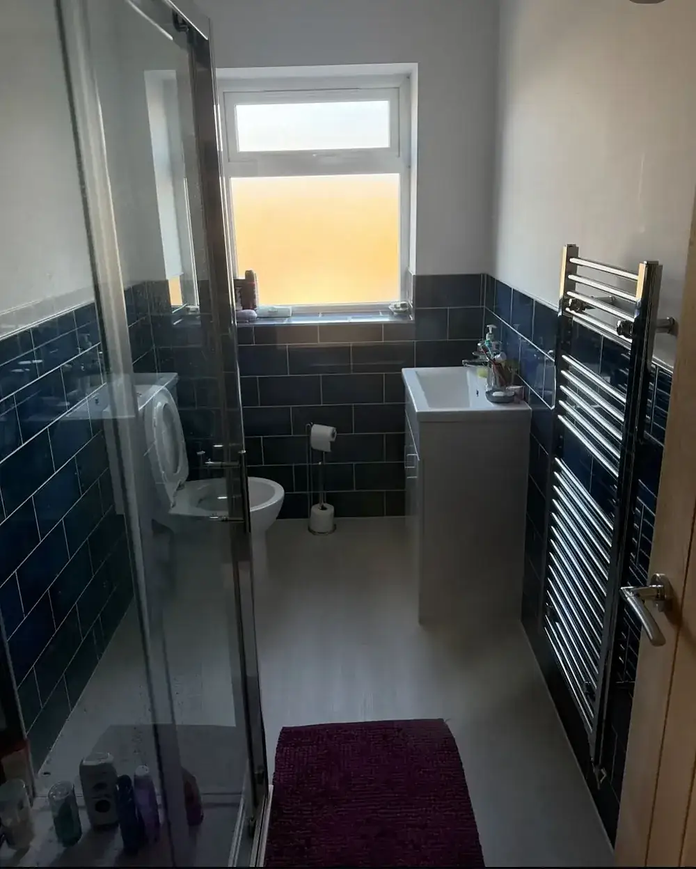Bathroom tiled in navy with a walk-in shower and heated towel rail