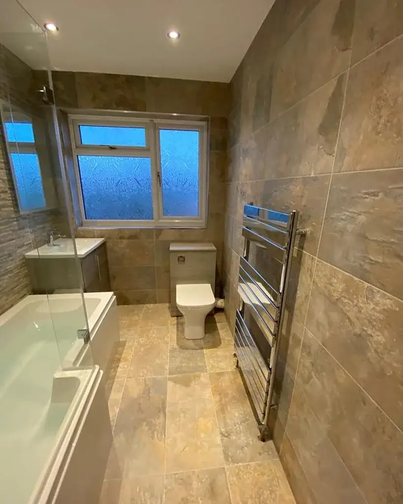Bathroom finished in stone-effect tiles with a bath and shower screen
