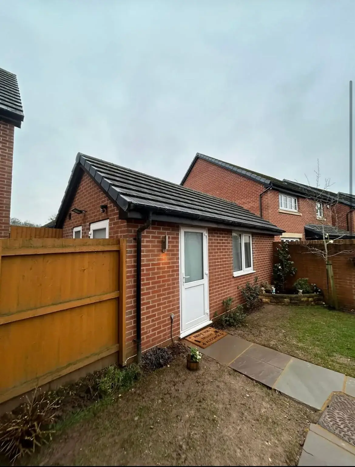 Brick outbuilding with a tiled roof beside a timber fence