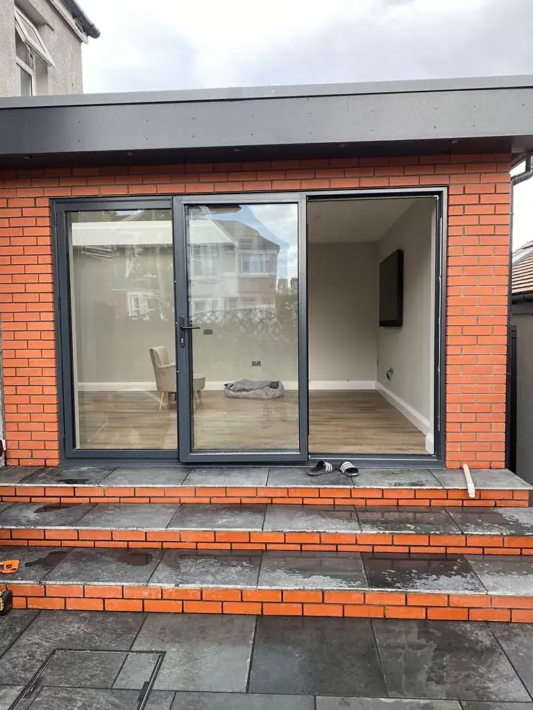 Red brick rear extension with grey sliding doors and brick steps down to the garden