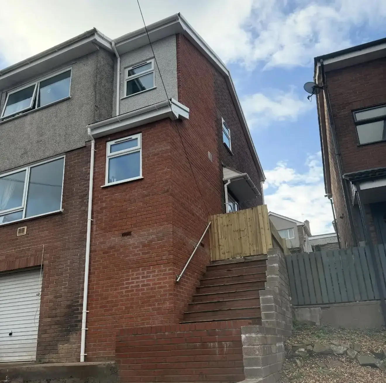 Brick steps with a handrail climbing beside a retaining wall at the rear of a house