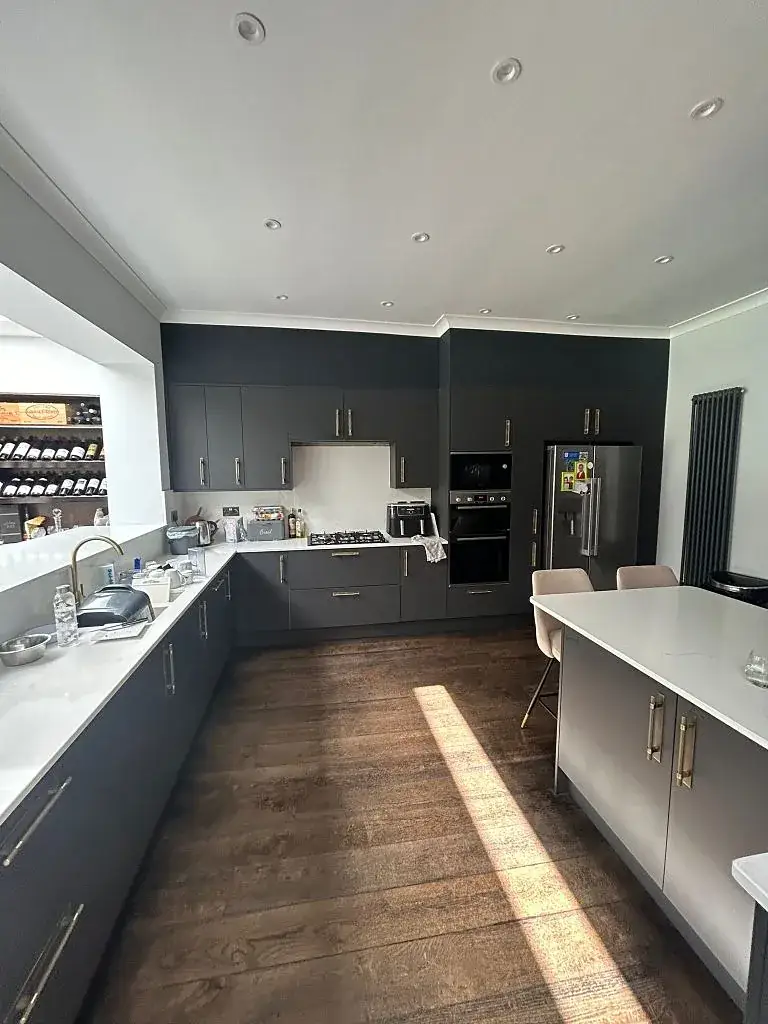 Graphite kitchen with white worktops, built-in ovens and a wooden floor