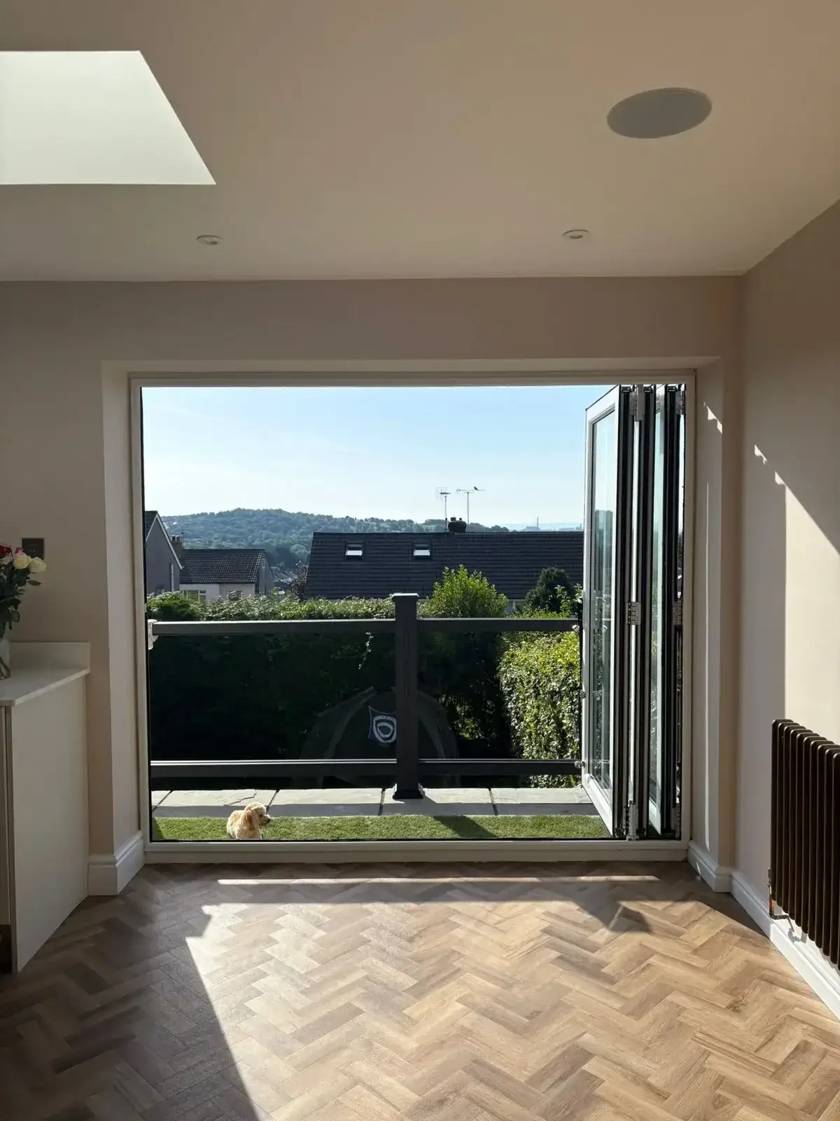 Bright room with herringbone flooring opening through bi-fold doors onto a terrace with a glass balustrade
