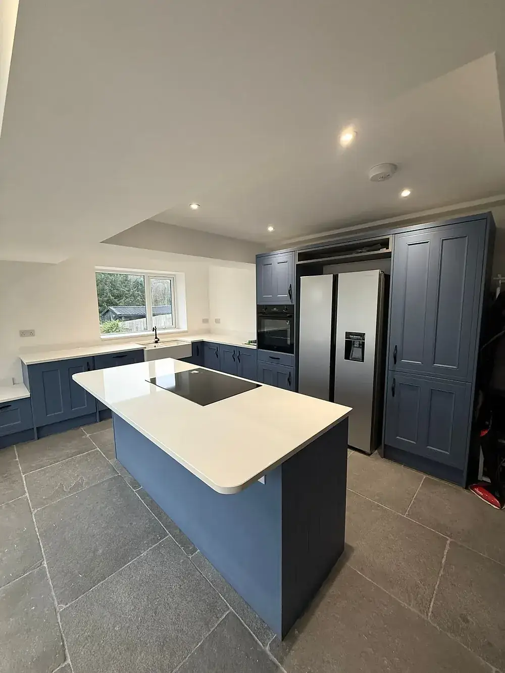 Navy kitchen with a pale stone island and an American-style fridge freezer