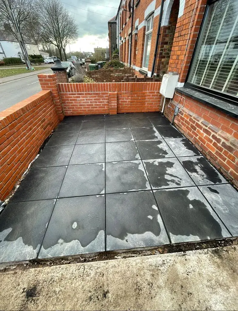 Walled courtyard laid with large dark porcelain paving slabs