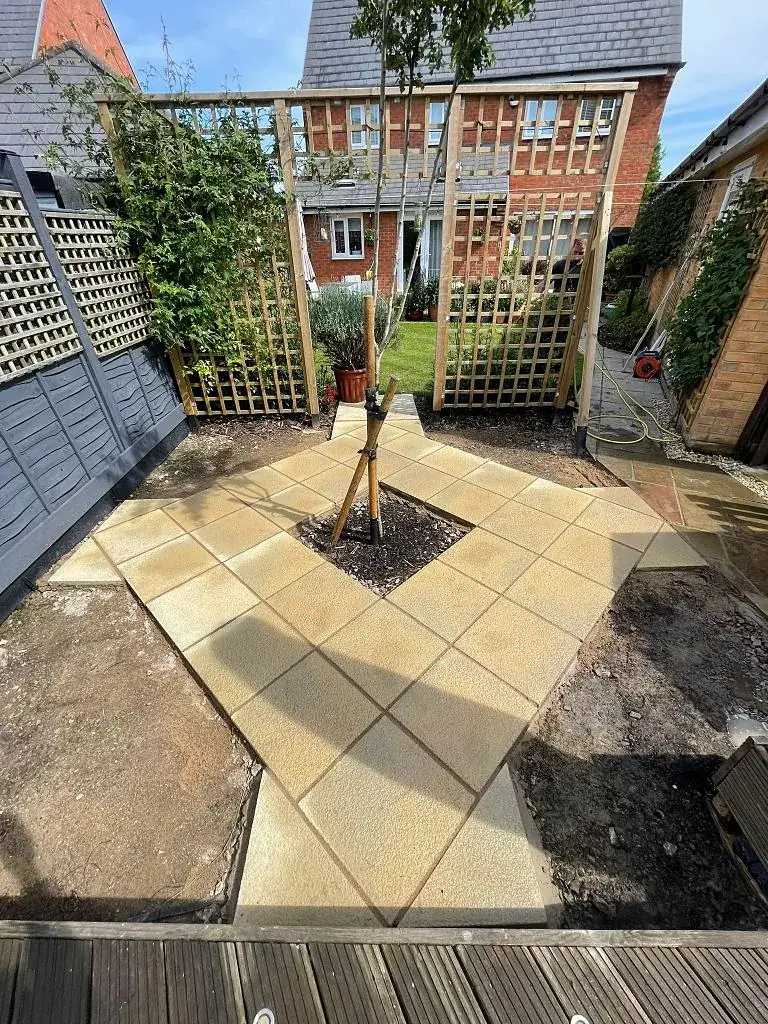 Sandstone paving laid around a young tree in a walled garden corner