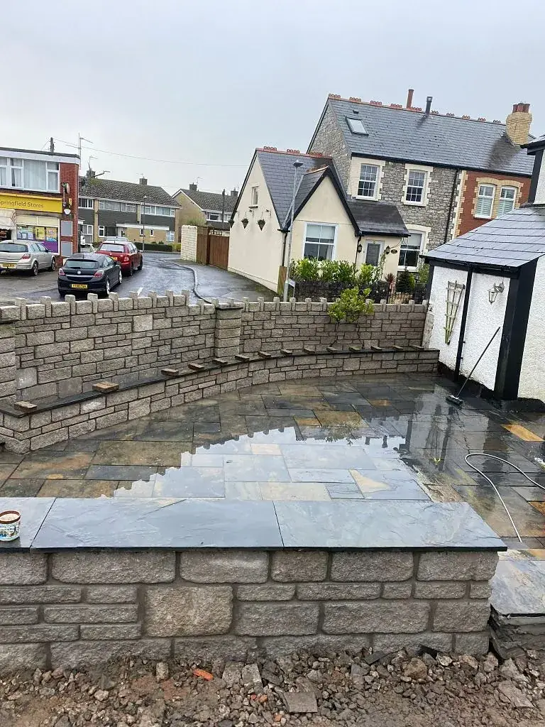Stone garden wall beside a newly laid patio, with village houses beyond